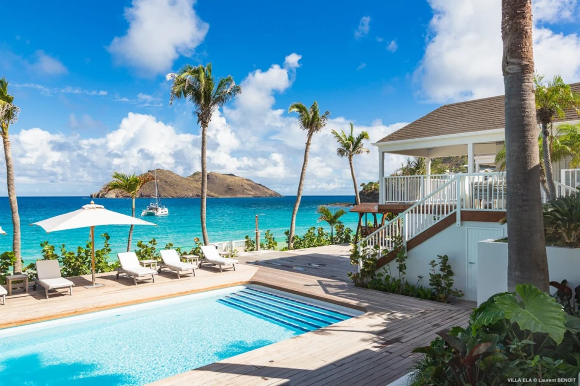 Luxurious villa with a swimming pool, sun loungers, and stunning views of the Caribbean Sea and an island in the background.