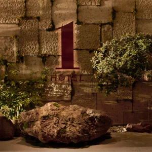 The sign for 1 Hotel Tokyo is displayed on a textured stone wall, flanked by rocks and greenery, creating a natural atmosphere.