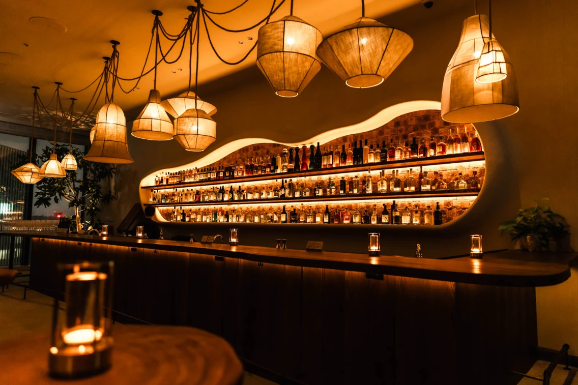 Stylish bar area with illuminated shelves displaying a variety of spirits, complemented by warm pendant lighting.