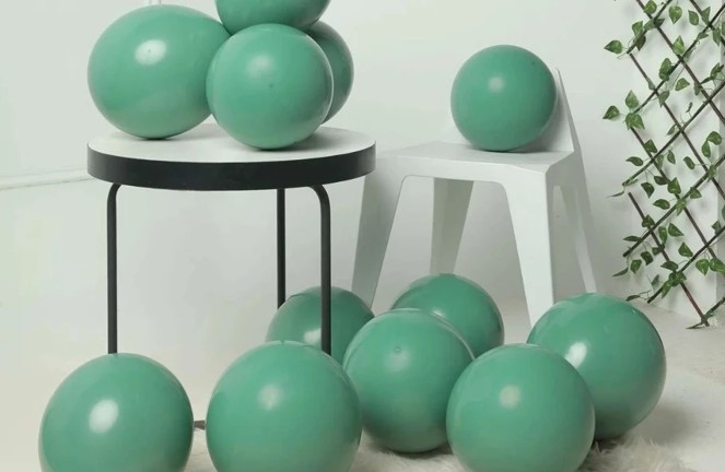 Green latex balloons scattered around a table and a chair in a bright, minimalist setting.