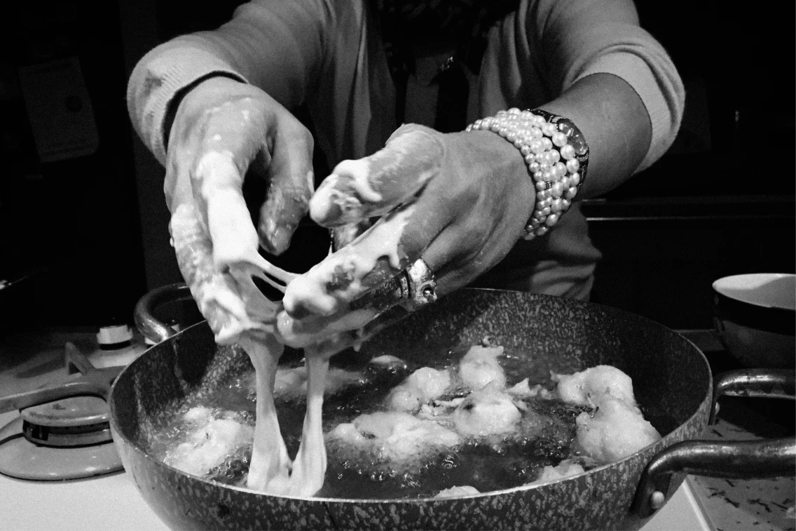 Hands covered in flour and dough pull apart or mix ingredients in a frying pan with bubbling oil.
