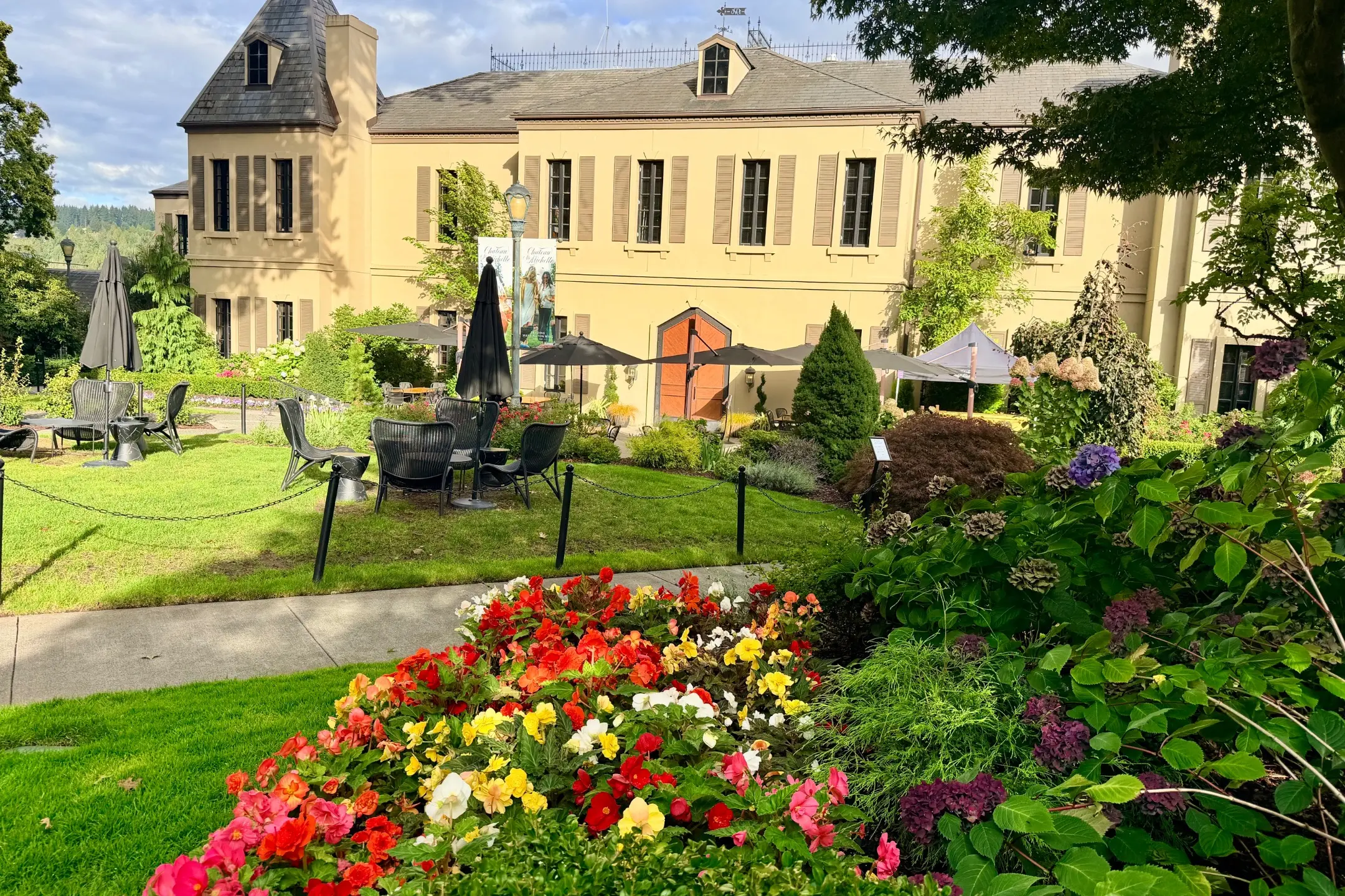 Colorful flower beds in the foreground with outdoor seating and the Chateau Ste. Michelle building in the background.