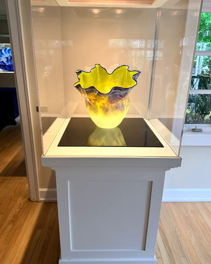 Colorful glass vase displayed in a showcase, featuring a wavy yellow rim and a blue accent along the edges.
