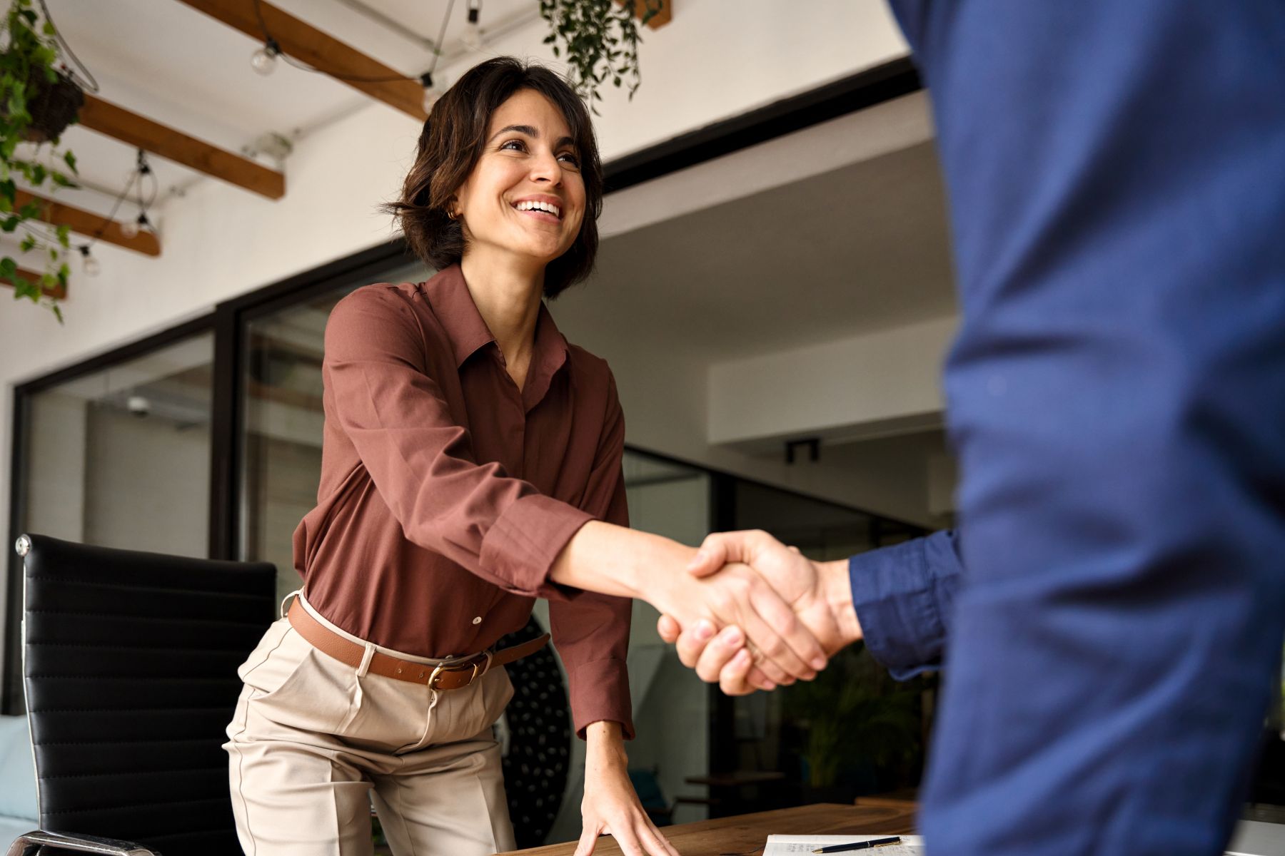 A smiling woman in professional attire shakes hands at a business meeting, embodying confidence and professionalism.