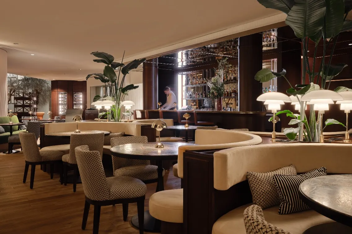 Stylish bar area at The Charles Hotel featuring elegant seating, plants, and a bartender preparing drinks.