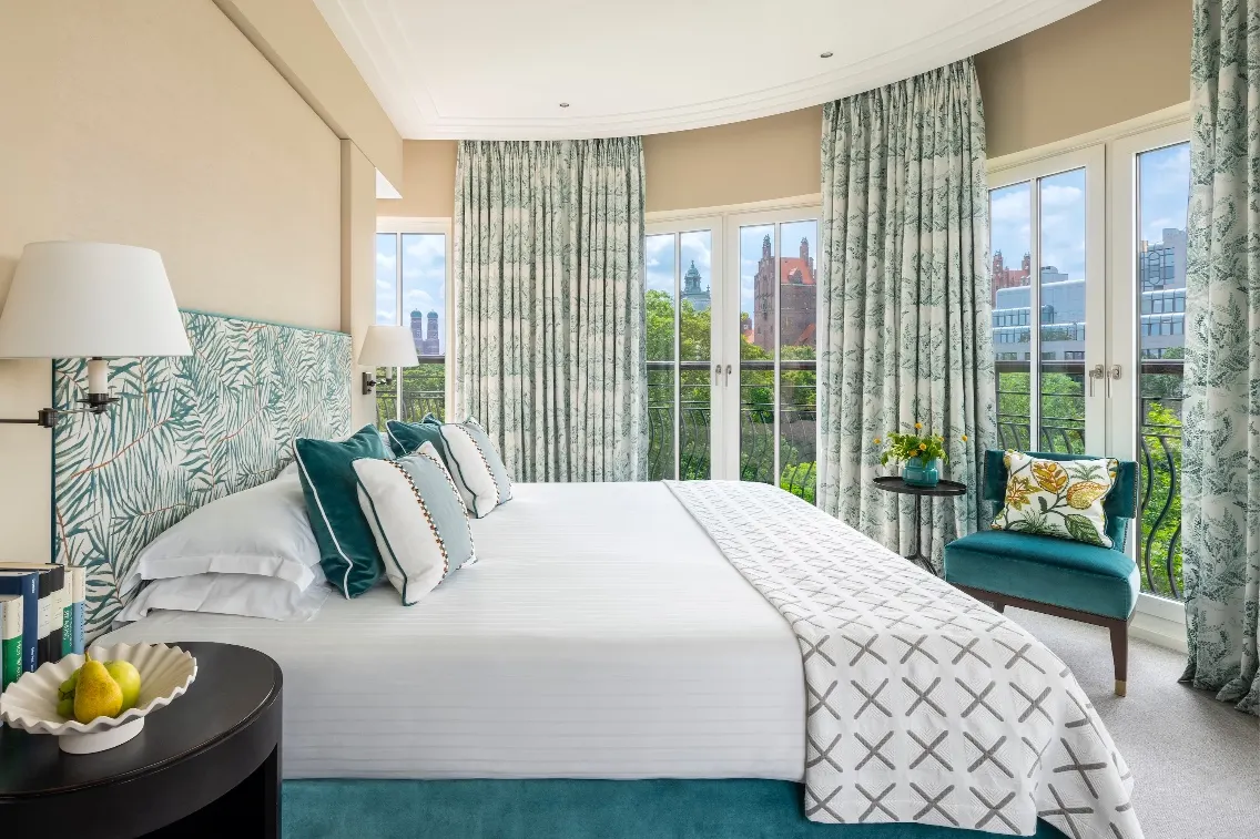 Elegant bedroom suite at The Charles, featuring lush decor, large windows, and a scenic view of the city.