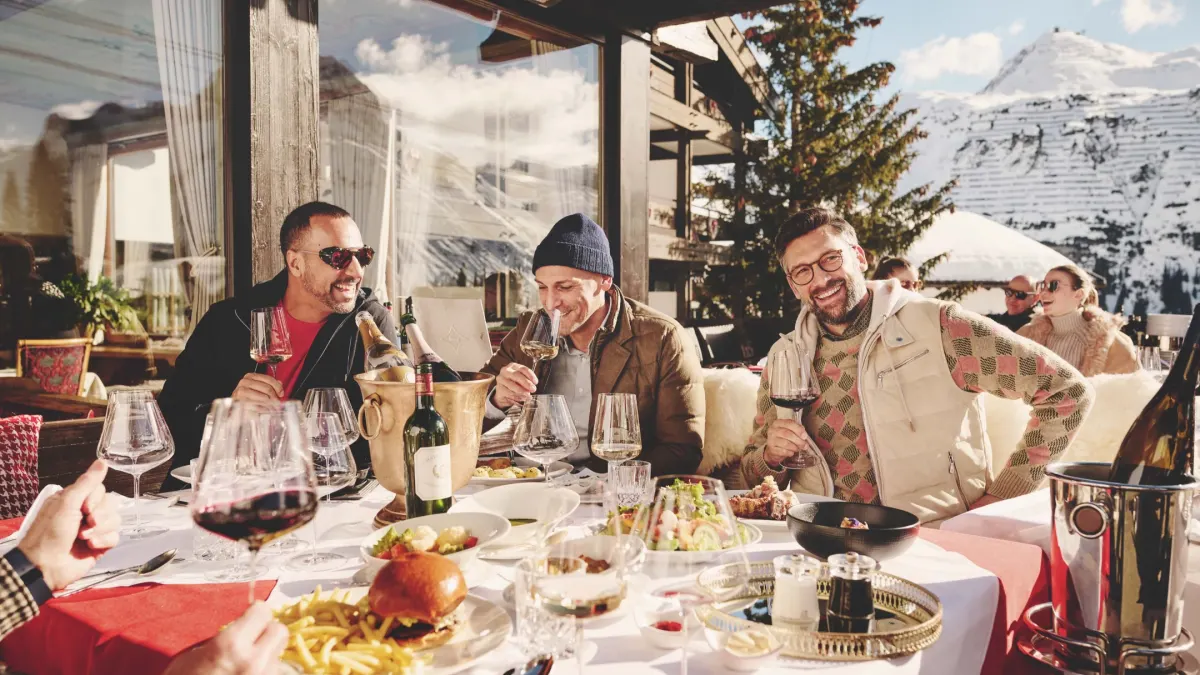 Friends enjoy a luxurious breakfast outdoors with mountain views, featuring gourmet dishes and fine wines.