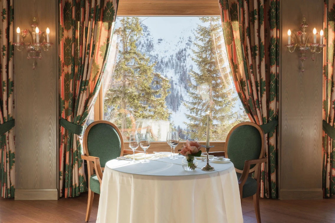 Elegant dining setup beside a window with snowy mountain views, featuring a white tablecloth and decorative floral centerpiece.