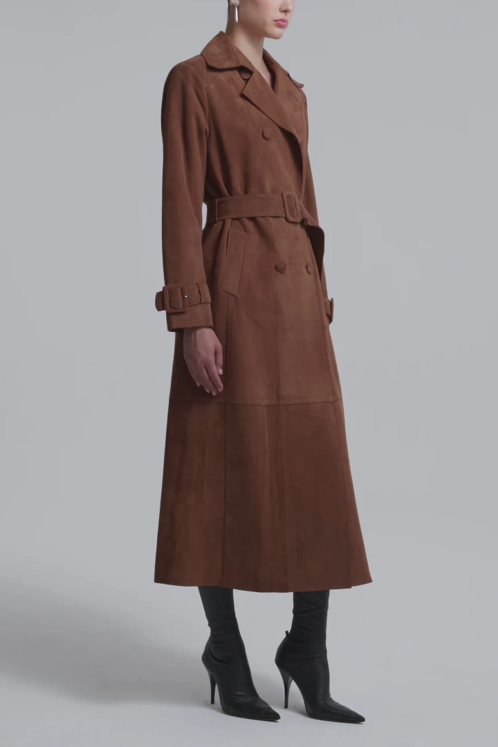 Brown suede trench coat with a belted waist, styled with tall black heeled boots and earrings, perfect for fall fashion.