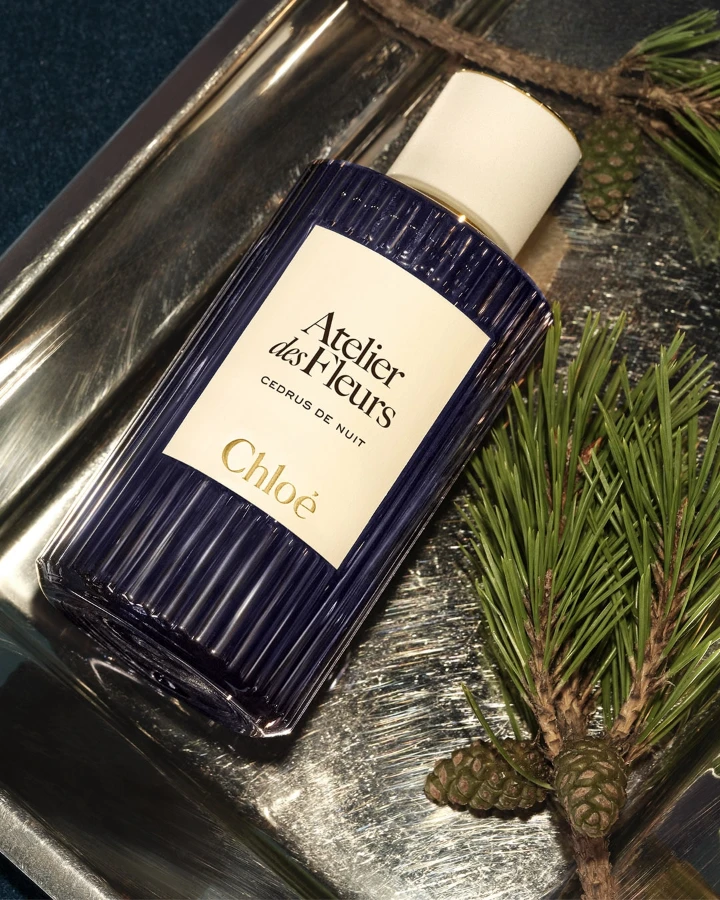 Chloé Atelier des Fleurs Cedrus de Nuit fragrance bottle surrounded by pine branches and pinecones on a silver tray.
