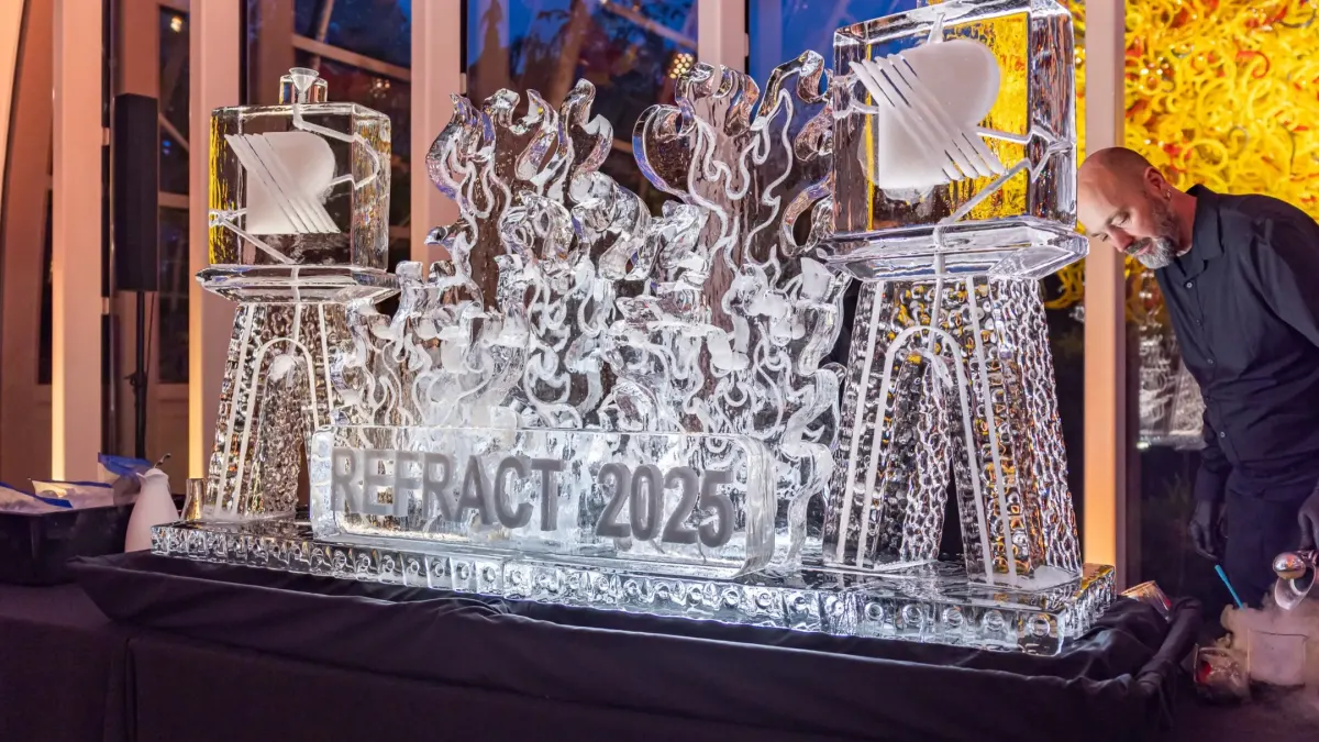 Intricate ice sculpture displaying "REFRACT 2025" with stylized flames, set up at Chihuly Garden and Glass for the opening night event.
