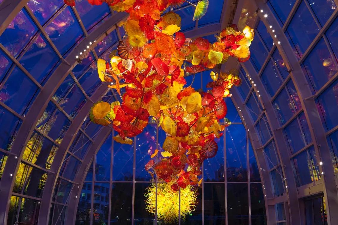 Colorful glass sculptures suspended from the ceiling of Chihuly Garden and Glass, illuminated against a dark blue background.