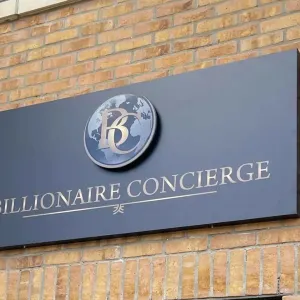 Billionaire Concierge sign on a brick wall, featuring a logo with a globe and the company name in elegant lettering.