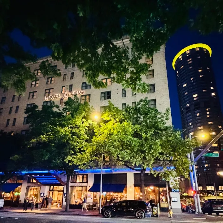Hotel Andra's illuminated sign at night, surrounded by trees, with a modern high-rise building in the background.