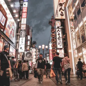 Bustling Osaka street lined with neon signs and shoppers exploring shops during twilight hours.