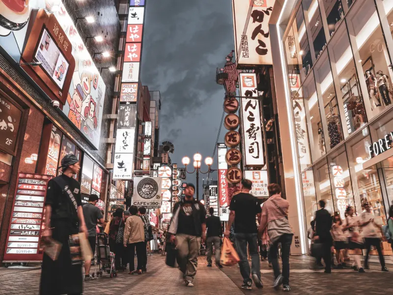 Bustling Osaka street lined with neon signs and shoppers exploring shops during twilight hours.