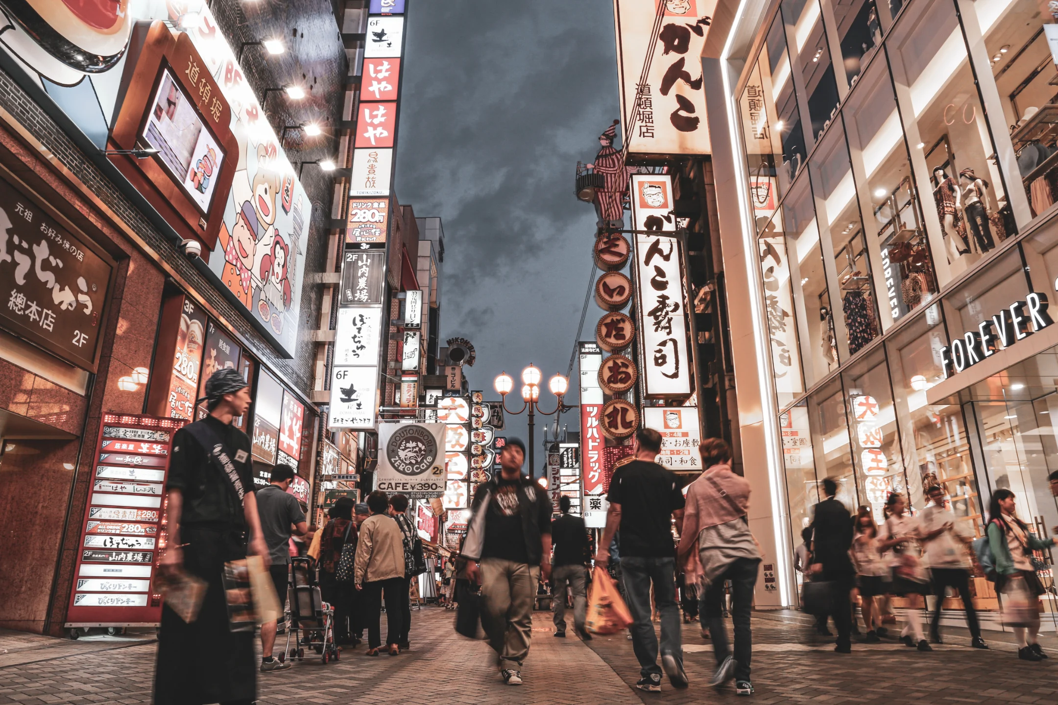 Bustling Osaka street lined with neon signs and shoppers exploring shops during twilight hours.