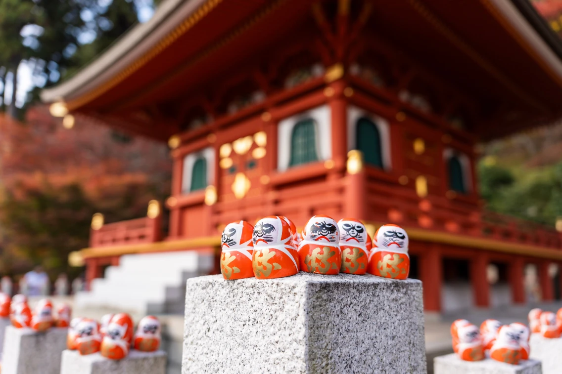 Daruma dolls are displayed in front of a traditional temple in Osaka, showcasing vibrant colors and intricate designs.