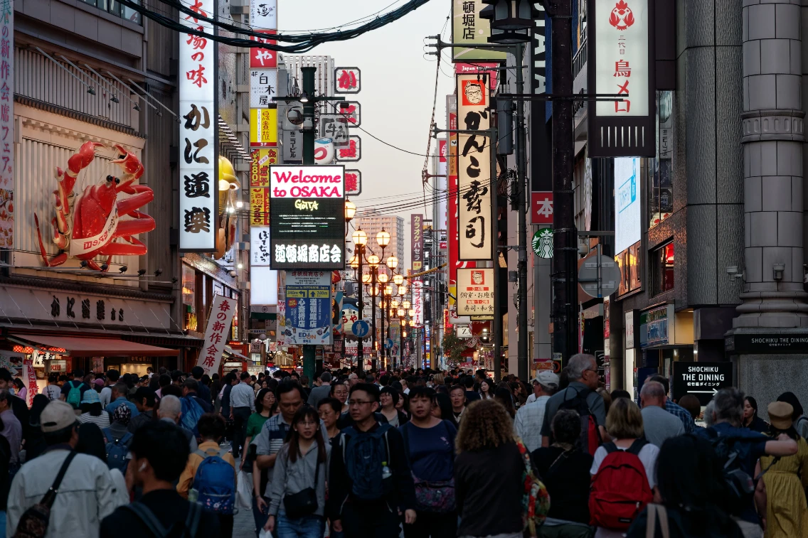 Busy street in Osaka illuminated by bright signs, with crowds of people enjoying the vibrant atmosphere during twilight.