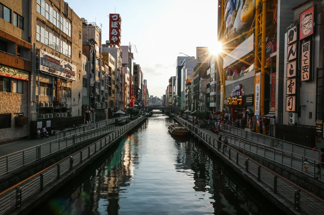 Sunset over Dotonbori canal, lined with neon-lit buildings and bustling walkways.