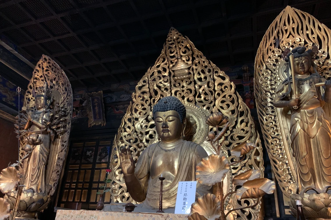 Golden Buddha statue with intricate carvings and figures of deities, set in a temple interior in Osaka.