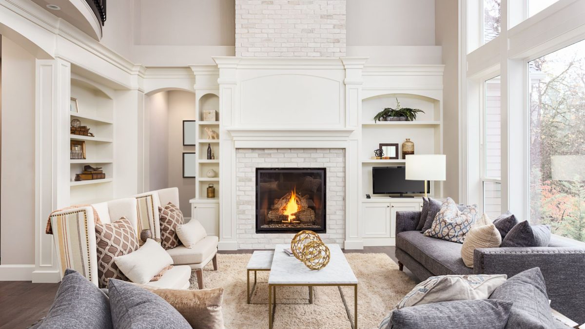 Cozy living room with a white brick fireplace, stylish furniture, and natural light from large windows.