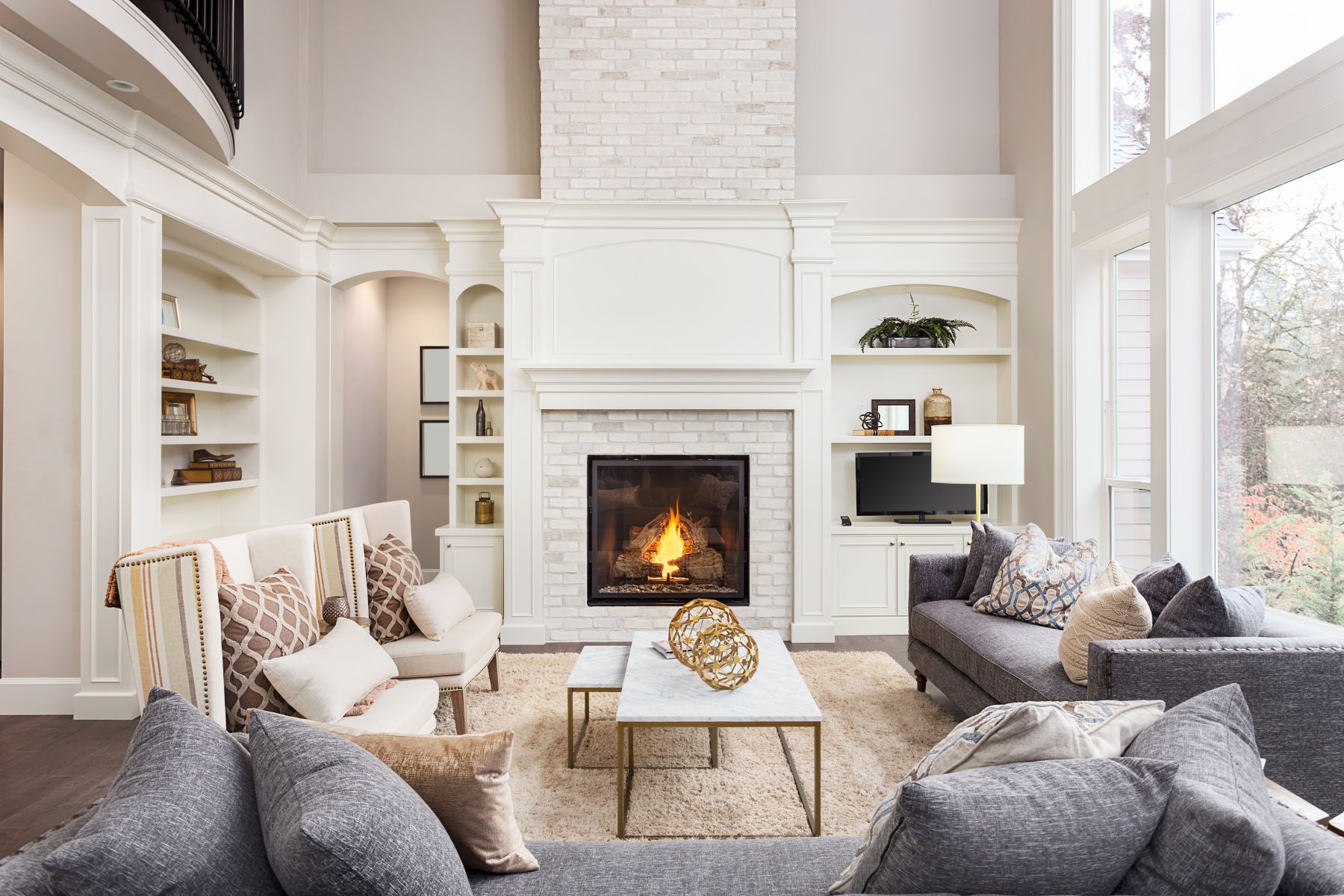 Cozy living room with a white brick fireplace, stylish furniture, and natural light from large windows.