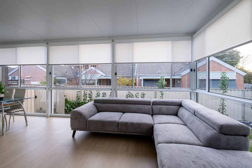 Modern living area with a grey sectional sofa, large windows, and light-filtering shades, enhancing light control and privacy.