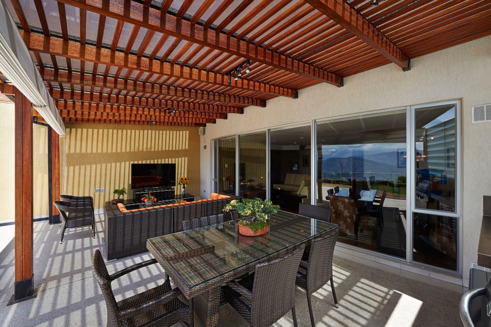 Stylish outdoor room featuring a dining table, comfortable seating, and a view through large glass windows.