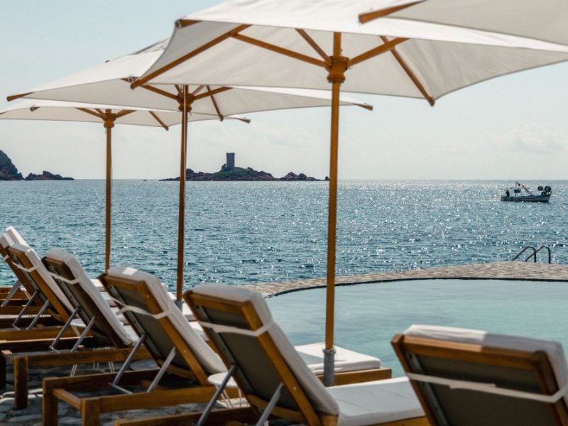 Lounge chairs with umbrellas overlook the sparkling Mediterranean Sea at Les Roches Rouges, a luxury hotel in the French Riviera.