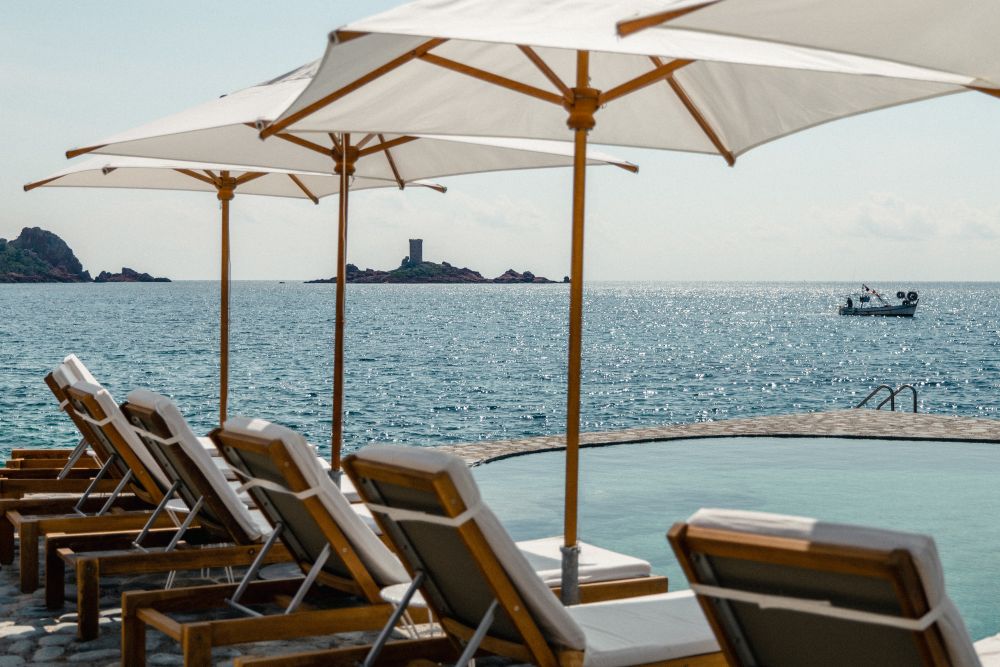 Lounge chairs with umbrellas overlook the sparkling Mediterranean Sea at Les Roches Rouges, a luxury hotel in the French Riviera.