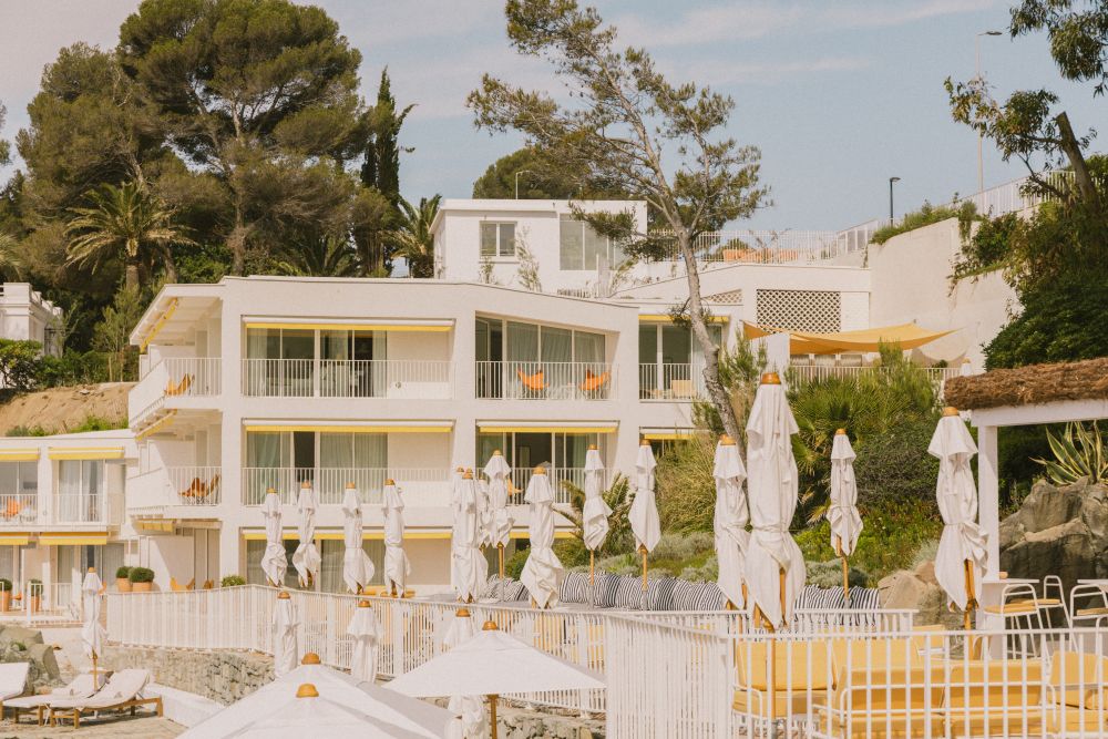 Luxury hotel Les Roches Rouges on the French Riviera, featuring white buildings, umbrellas, and lush greenery by the Mediterranean.