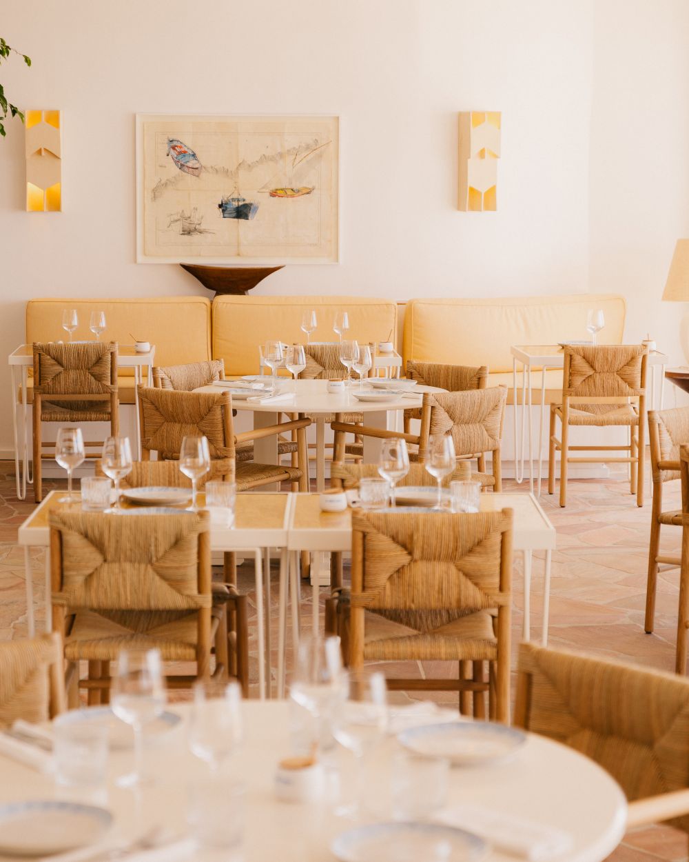 Stylish dining area at Les Roches Rouges featuring woven chairs, elegant table settings, and nautical artwork on the walls.