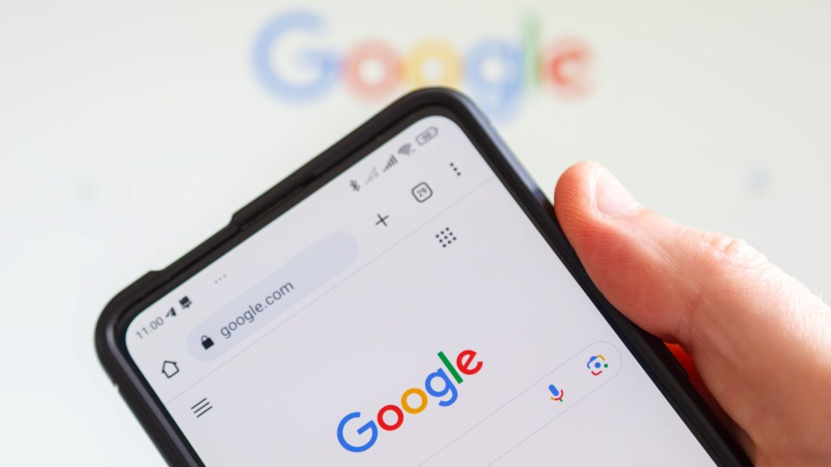 A hand holding a smartphone displaying the Google search page.
