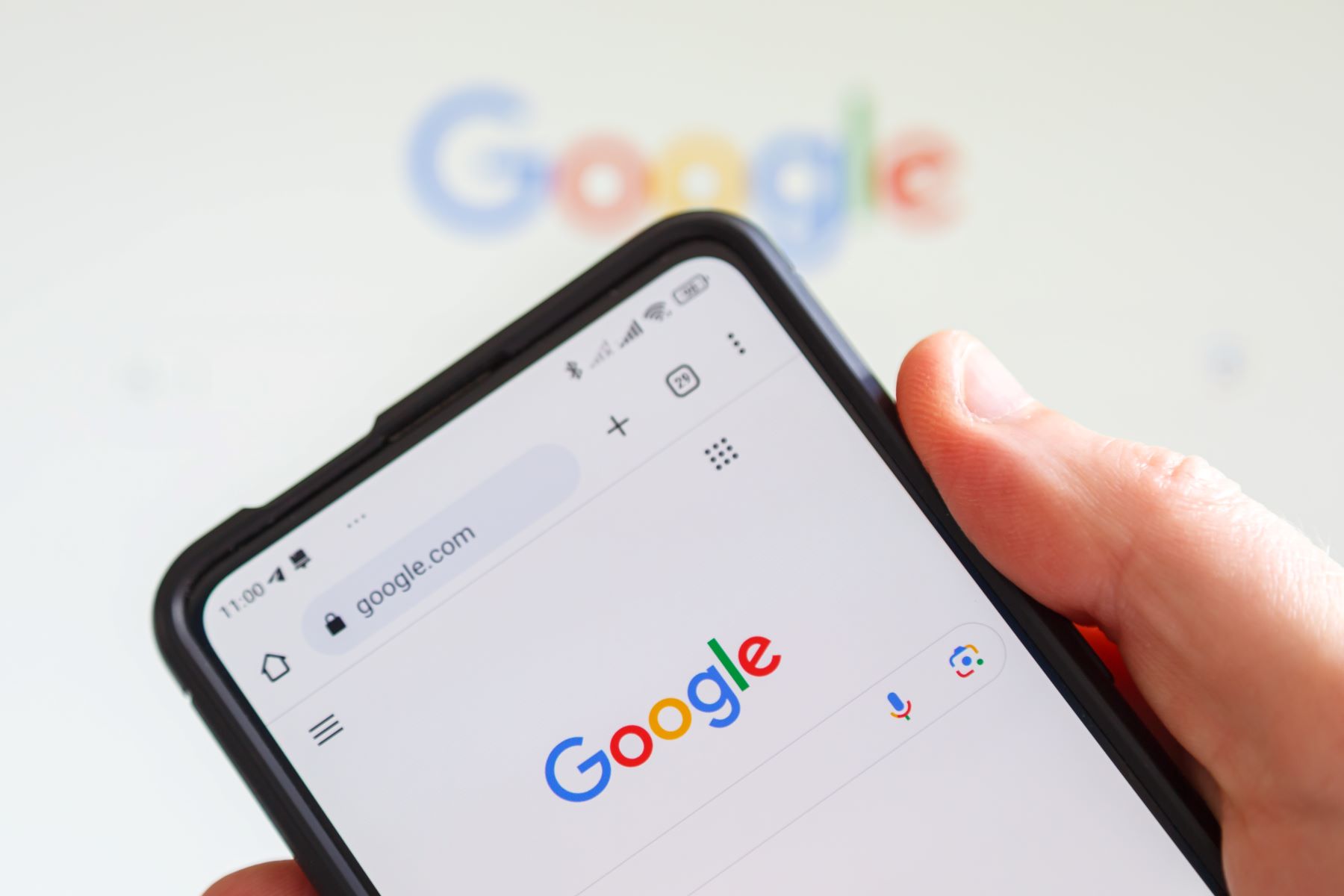 A hand holding a smartphone displaying the Google search page.