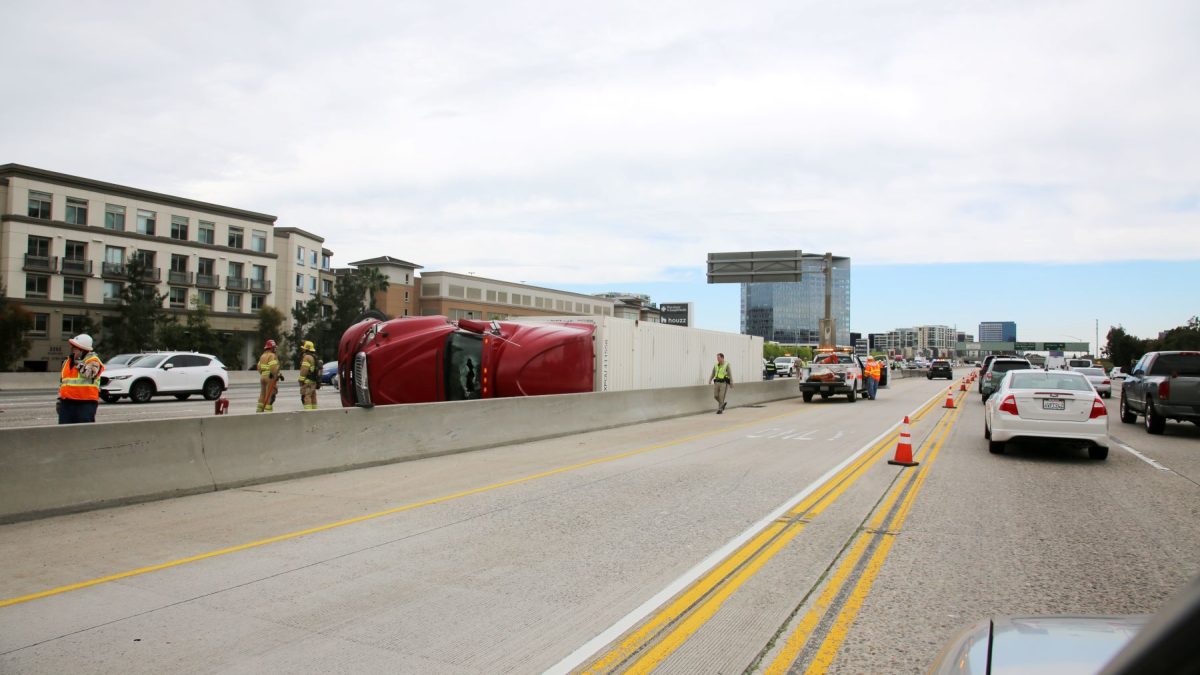 Red truck overturned on a highway as emergency personnel work to manage the scene and traffic is diverted.