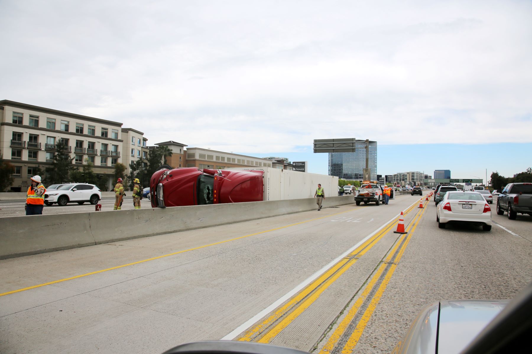 Red truck overturned on a highway as emergency personnel work to manage the scene and traffic is diverted.