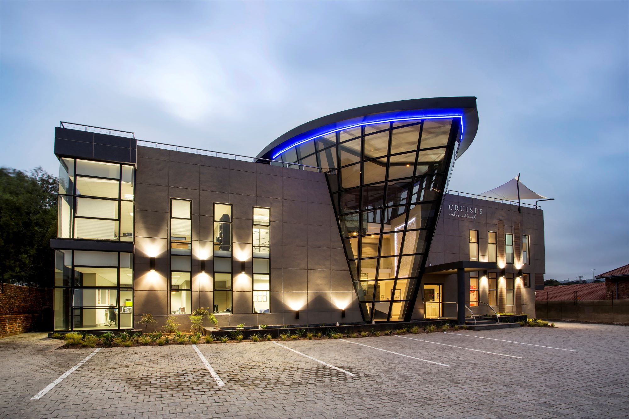 Modern architectural design featuring dynamic lines and illuminated glass elements against an evening sky.