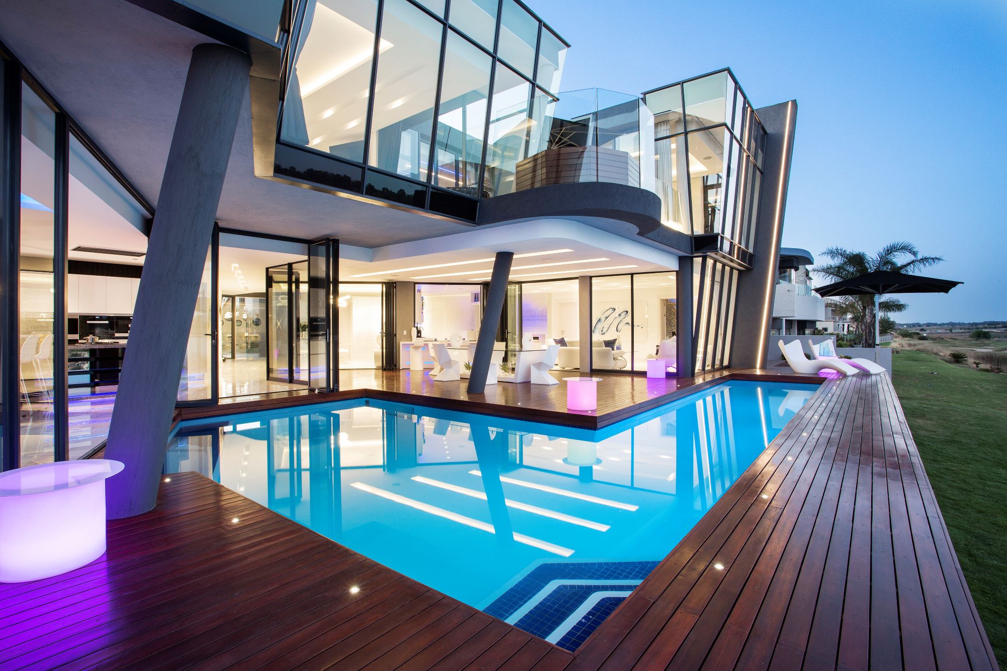 Modern architecture featuring large glass windows, a swimming pool, and sleek design elements illuminated by ambient lighting.