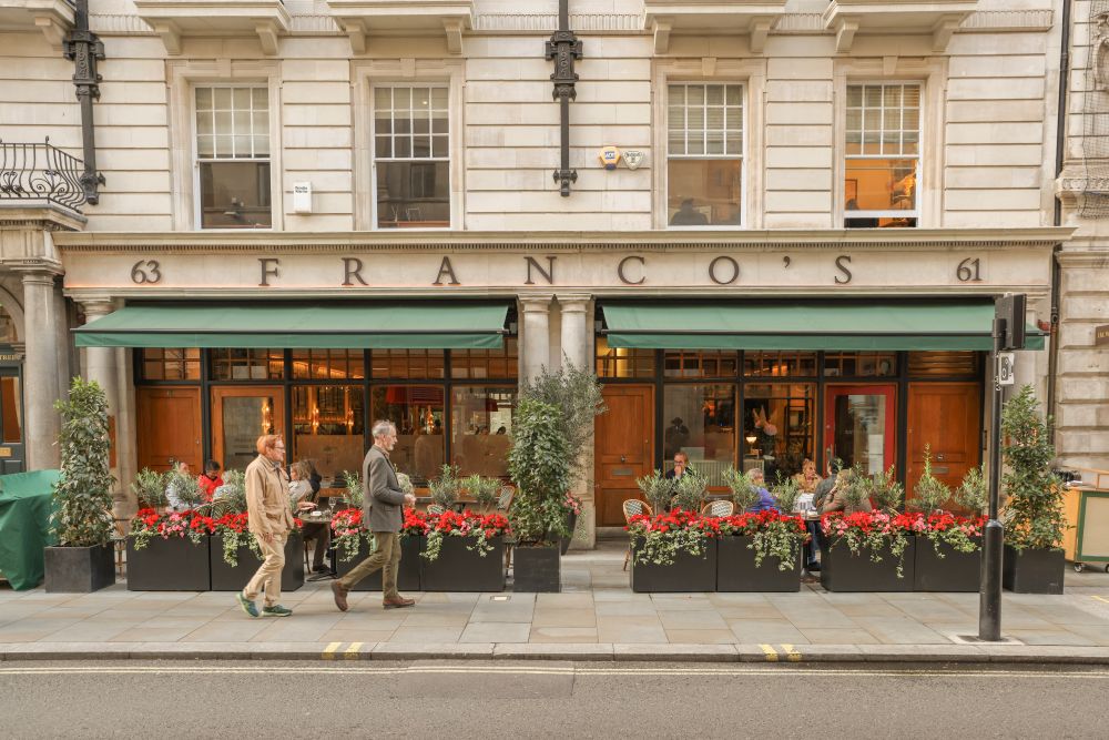 Franco's restaurant exterior in Mayfair, featuring outdoor seating adorned with vibrant flowers on a busy street.