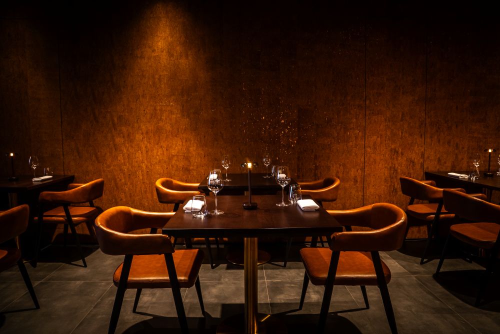Elegant dining setup with dark wooden walls, cozy chairs, and candlelit tables, creating an intimate atmosphere for meals.
