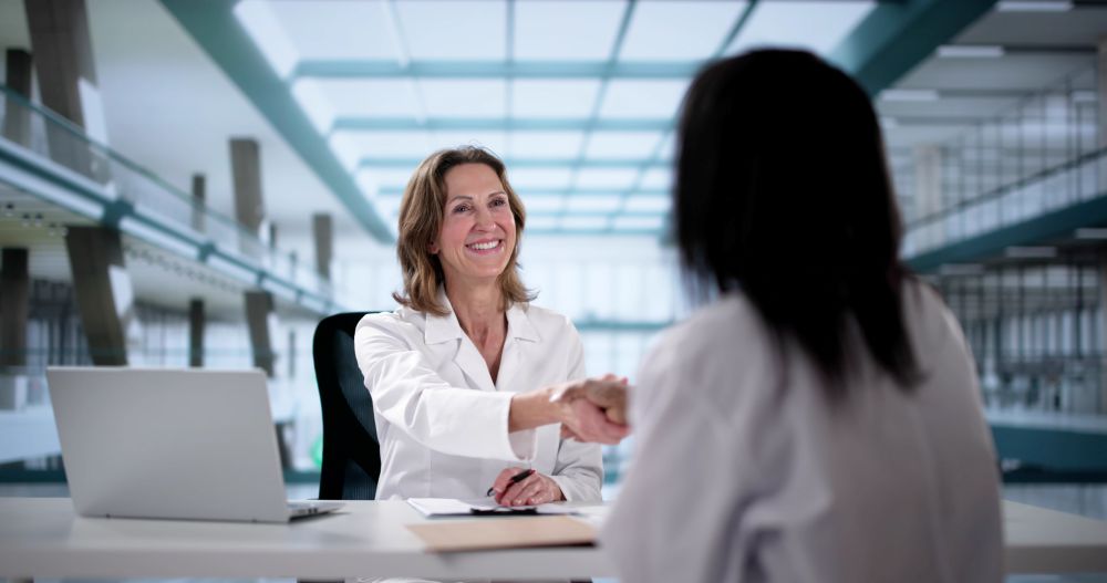Healthcare professional smiling and shaking hands with another in a modern office setting.
