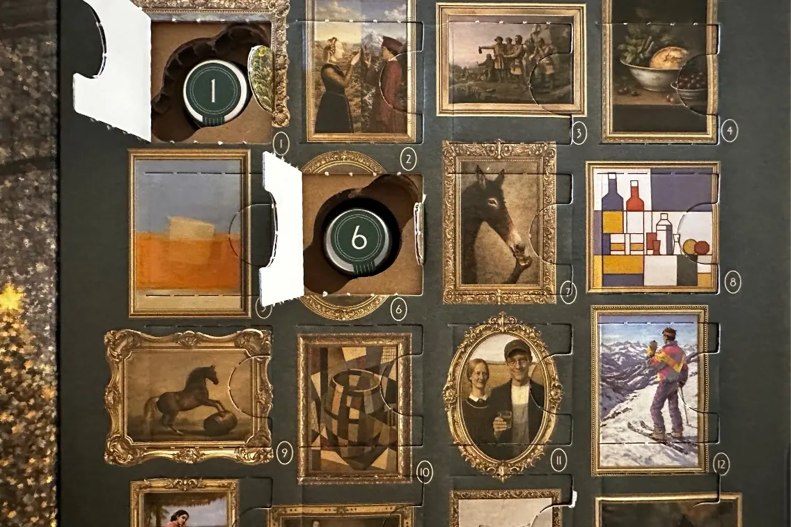 An advent calendar with various art frames and a whiskey bottle behind one of the doors, themed for the holiday season.