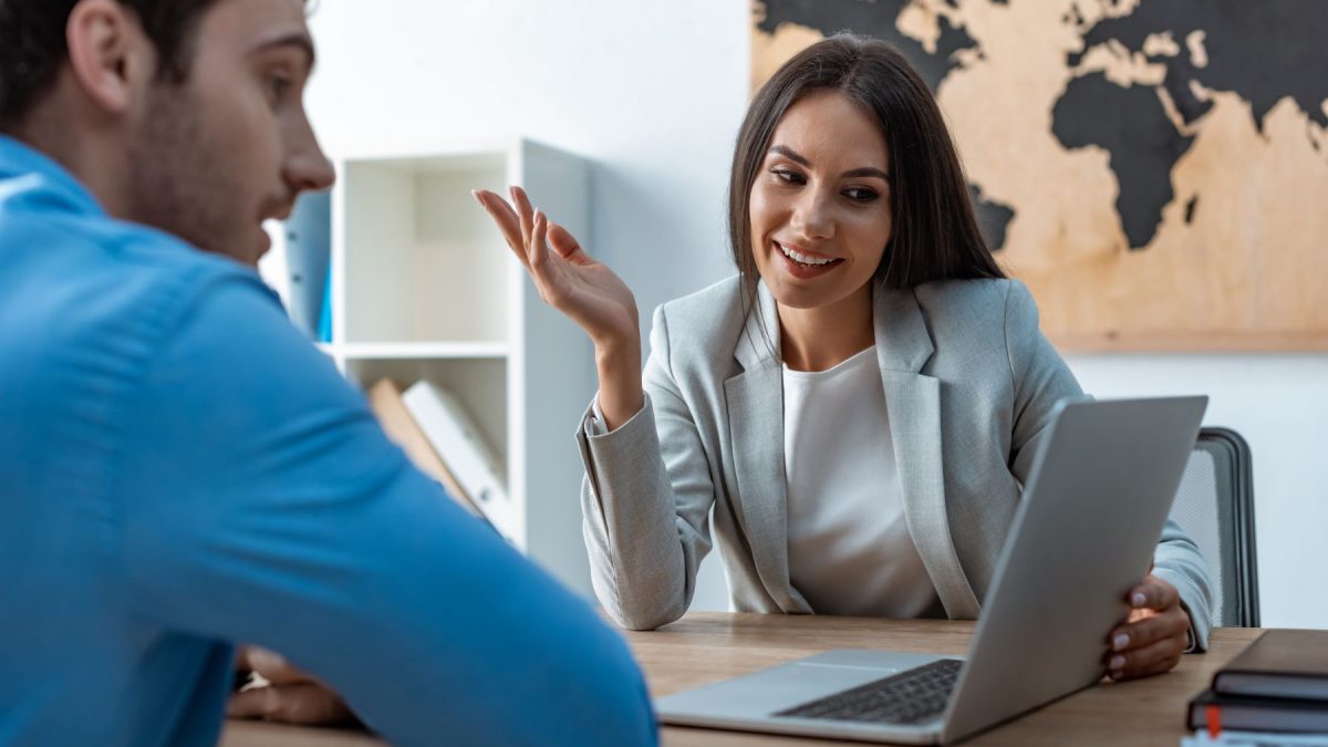 Business meeting between a man and woman, discussing corporate travel plans with a laptop on the table.