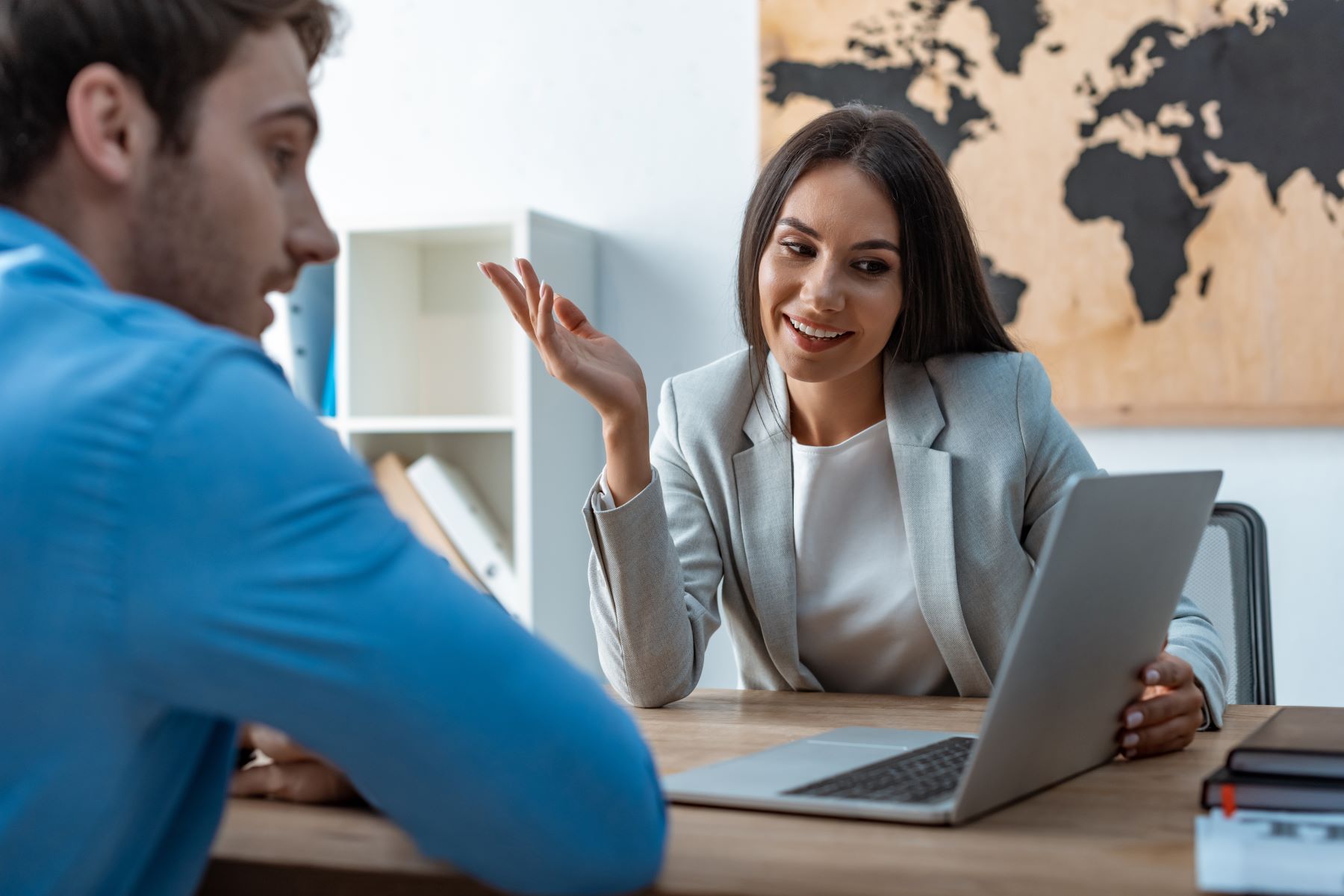 Business meeting between a man and woman, discussing corporate travel plans with a laptop on the table.