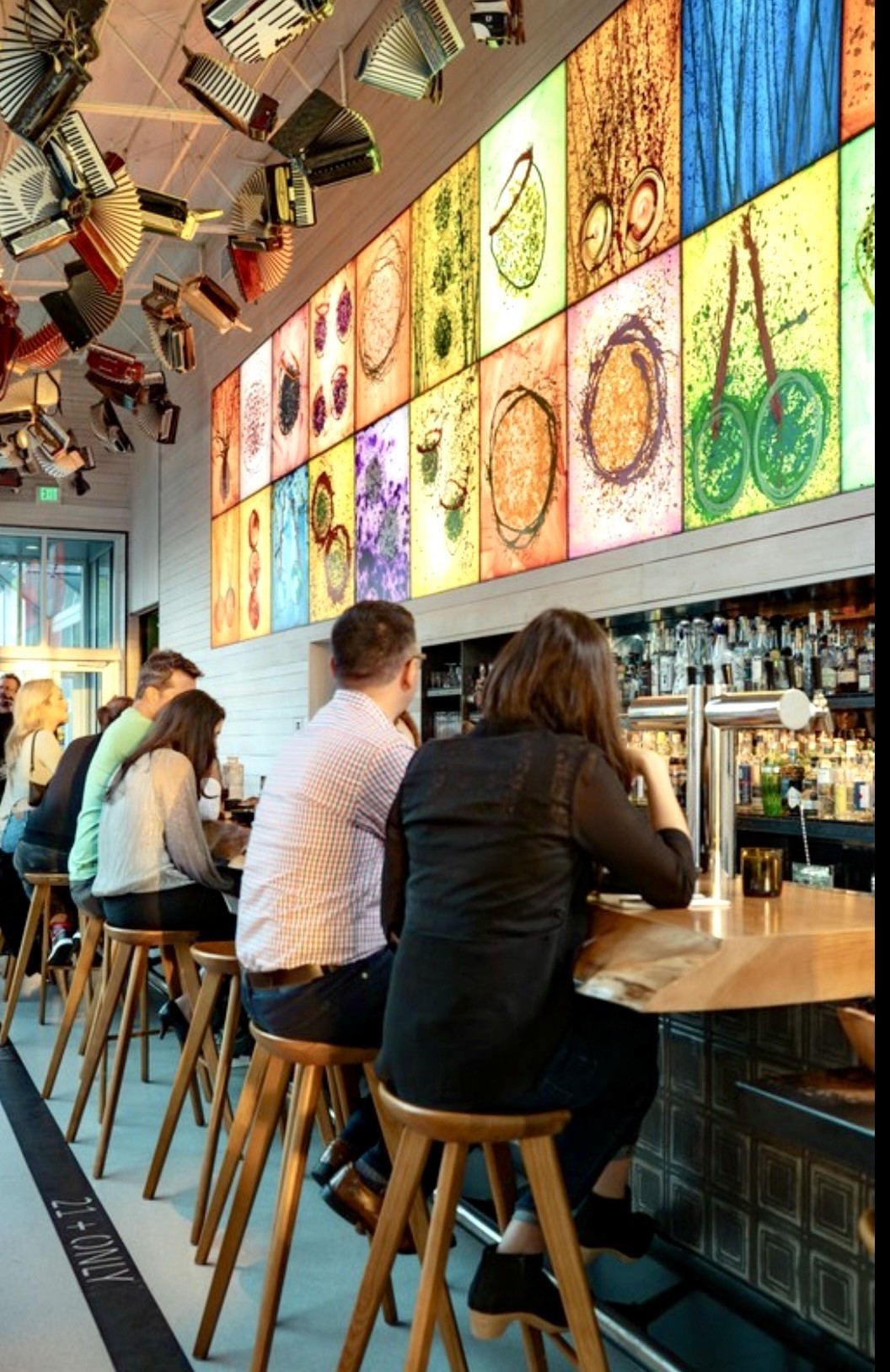Guests enjoy drinks at a bar with a vibrant, artistic wall display featuring colorful glass-inspired artwork.