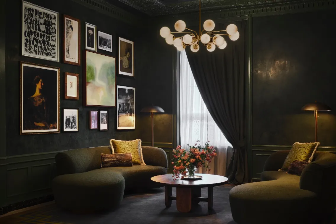 Cozy lobby sitting area featuring dark walls, elegant artwork, plush seating, and a stylish chandelier.