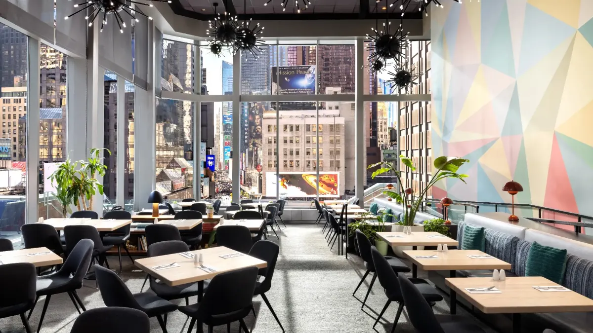 Modern restaurant interior with vibrant decor and large windows showcasing a bustling Times Square view.