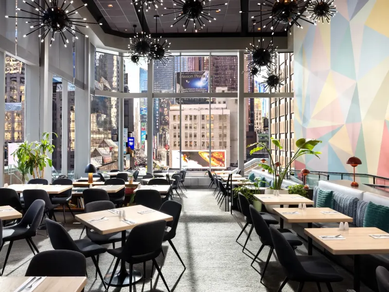 Modern restaurant interior with vibrant decor and large windows showcasing a bustling Times Square view.