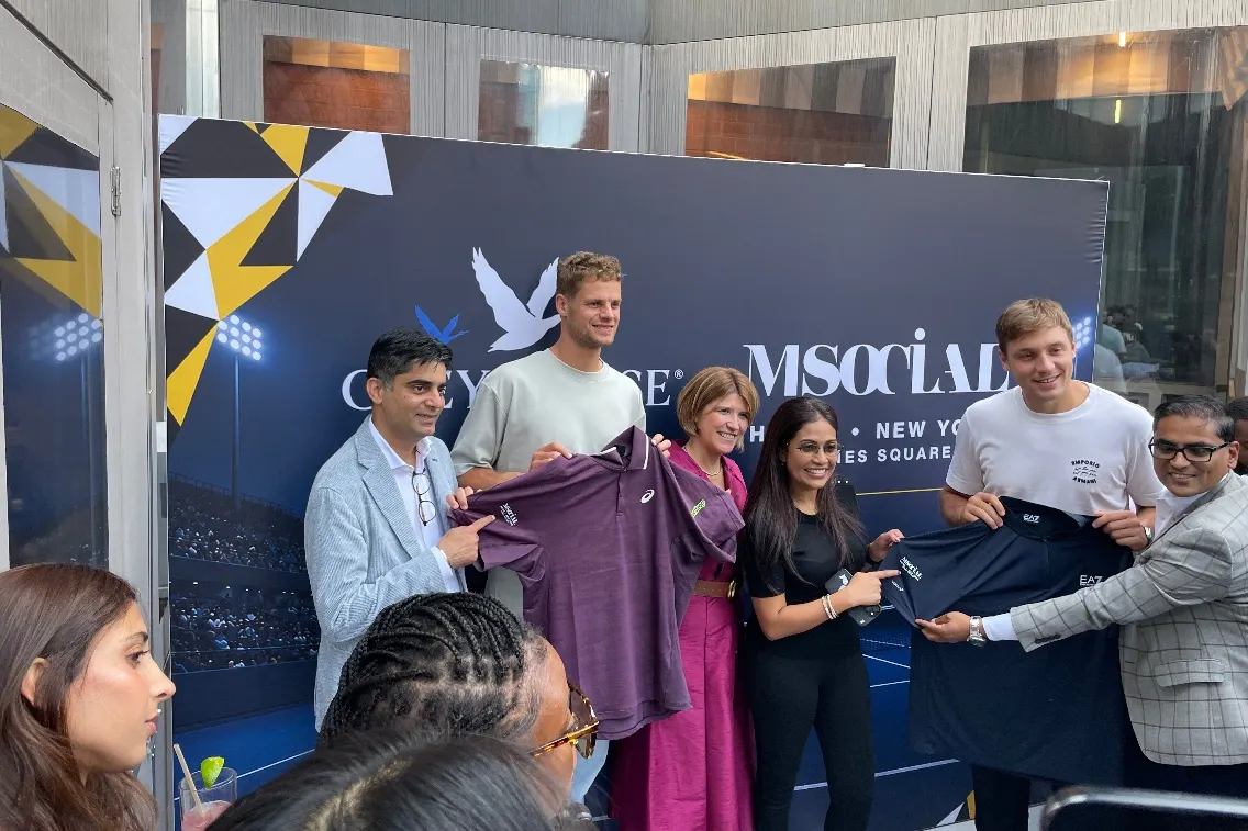 Participants at a promotional event hold up branded t-shirts in front of a backdrop featuring M Social Times Square.